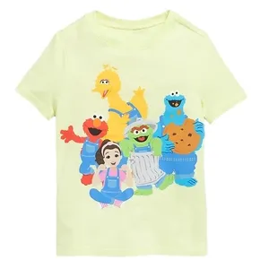 A light yellow t-shirt featuring colorful characters including a yellow bird, red monster, blue monster with cookies, green character in a trash can, and a cartoon girl.