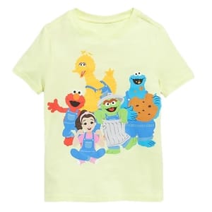 A light yellow t-shirt featuring colorful characters including a yellow bird, red monster, blue monster with cookies, green character in a trash can, and a cartoon girl.