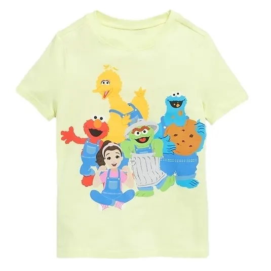 A light yellow t-shirt featuring colorful characters including a yellow bird, red monster, blue monster with cookies, green character in a trash can, and a cartoon girl.