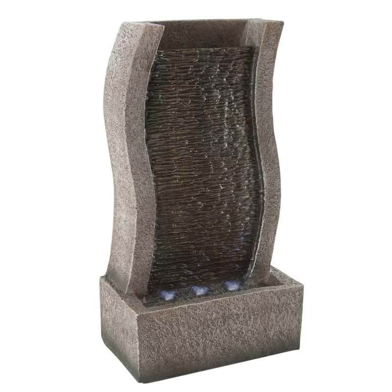 A freestanding indoor water fountain with a stone-like texture and a curved design, including a visible water cascade over a ribbed surface.