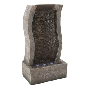 A freestanding indoor water fountain with a stone-like texture and a curved design, including a visible water cascade over a ribbed surface.