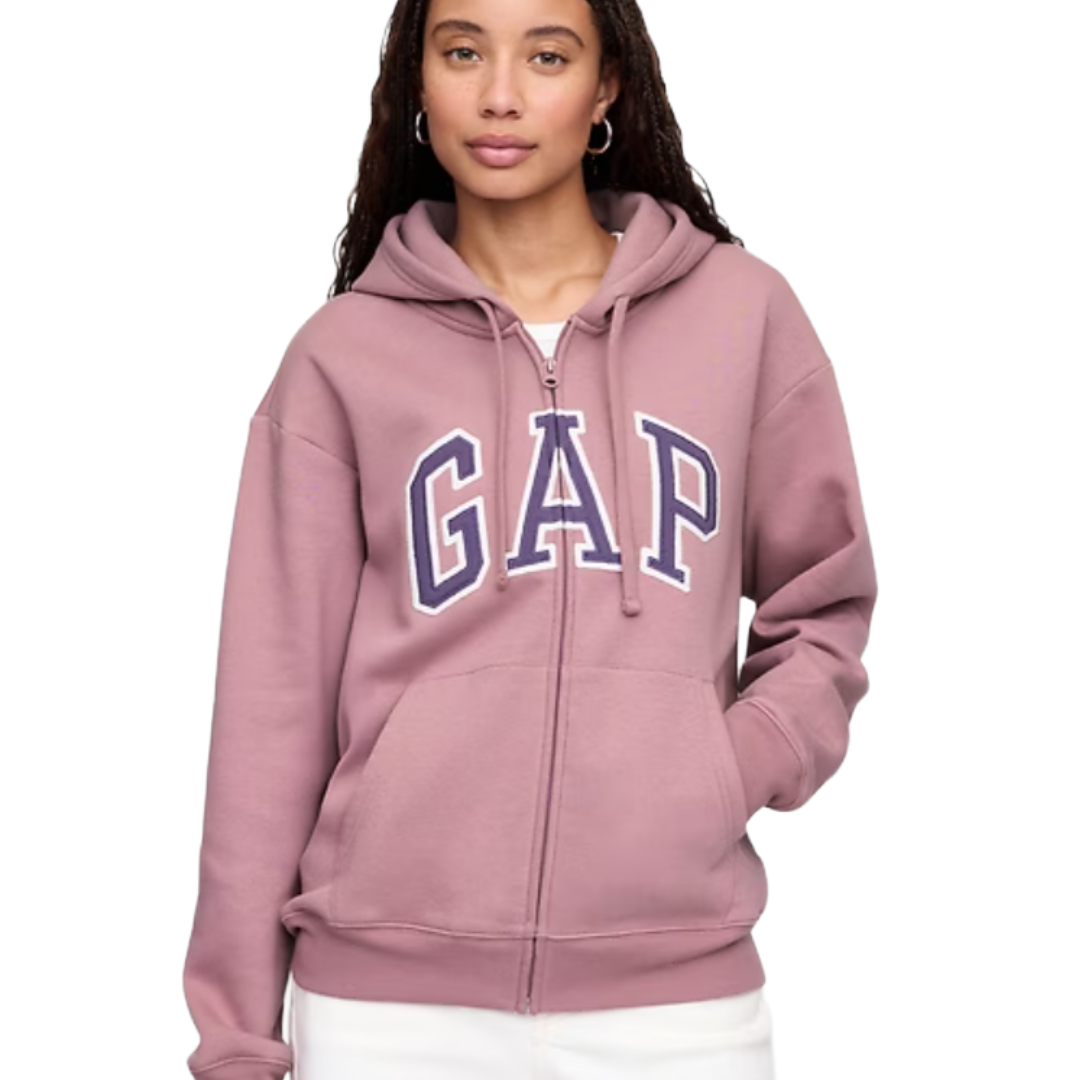 A person wears a mauve zip-up hoodie with the word \“GAP\“ in bold blue and white letters on the front, paired with white pants.