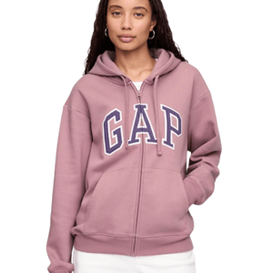 A person wears a mauve zip-up hoodie with the word \“GAP\“ in bold blue and white letters on the front, paired with white pants.