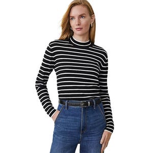 A woman wearing a black and white striped long-sleeve top with a high collar, paired with blue high-waisted jeans and a black belt.