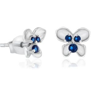Silver stud earrings shaped like flowers feature three small round blue stones at each center. The petals have a smooth, reflective finish, complementing the vibrant blue gems.