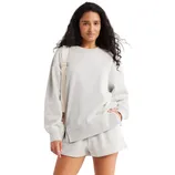 A woman wearing a light gray crewneck sweatshirt paired with matching shorts, carrying a white strap bag.