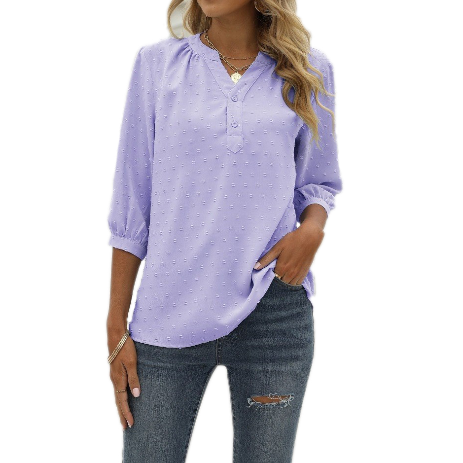 A woman is wearing a light purple textured blouse with 3/4 sleeves and button details, paired with distressed blue jeans. She accessorizes with layered necklaces and a bracelet.