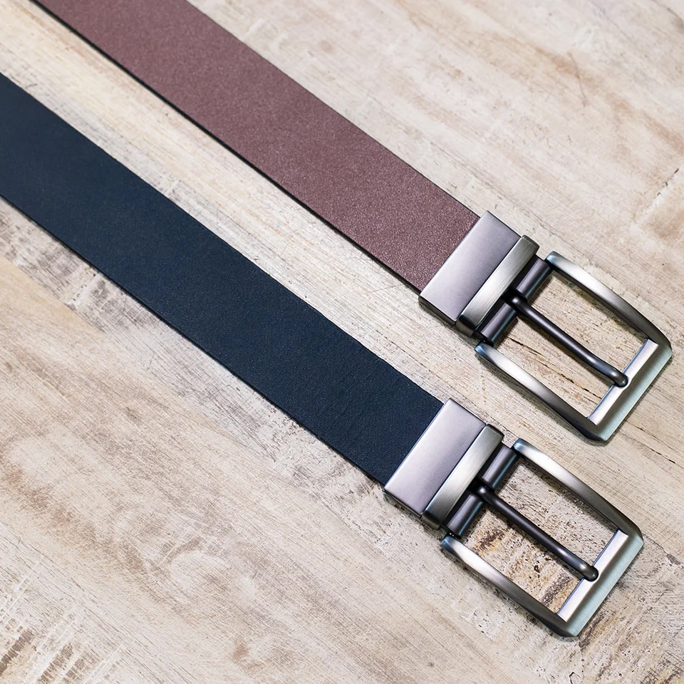 Two 1.25-inch leather belts shown on a wooden surface, one in brown and the other in black, both featuring metal buckles with a brushed silver finish.