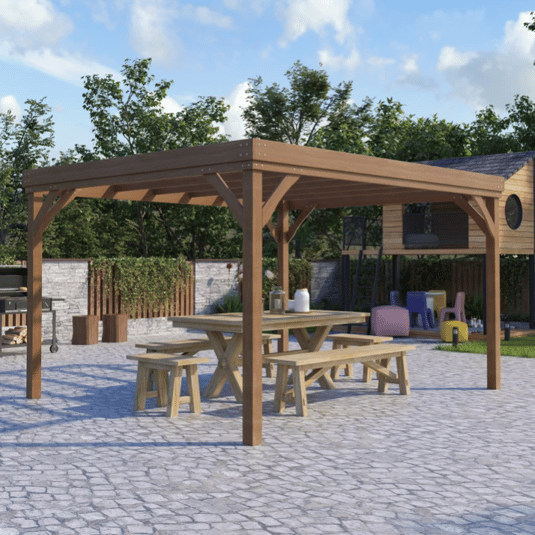 A wooden outdoor pergola with a picnic table and benches underneath, set on a stone patio. A grill is on the left, and there's a children's play area with colorful chairs in the background.