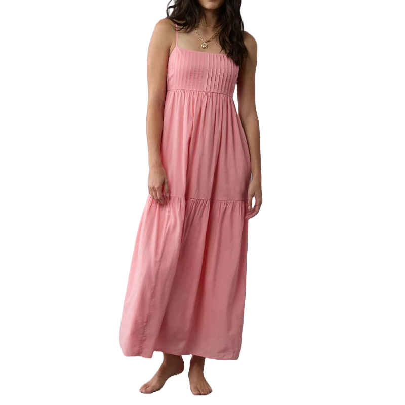 A woman is wearing a pink sleeveless maxi dress with thin straps and a flowy, tiered skirt.
