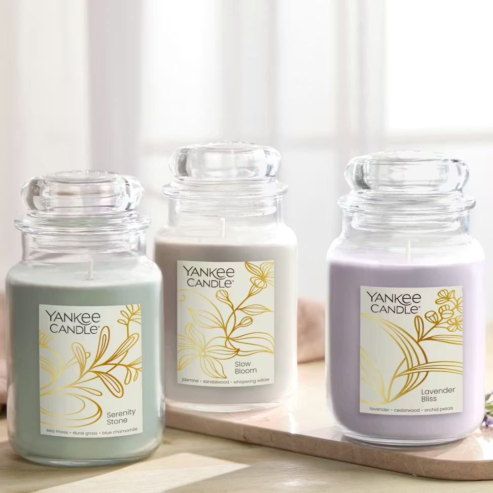 Three Yankee Candle jars are shown: Serenity Stone (sea moss, dune grass, blue chamomile), Slow Bloom (jasmine, sandalwood, whispering willow), and Lavender Bliss (lavender, cedarwood, orchid petals).