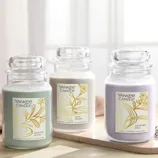 Three Yankee Candle jars are shown: Serenity Stone (sea moss, dune grass, blue chamomile), Slow Bloom (jasmine, sandalwood, whispering willow), and Lavender Bliss (lavender, cedarwood, orchid petals).