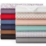 A stack of folded bed sheets in various solid colors and patterns, including floral, geometric, and checked designs.