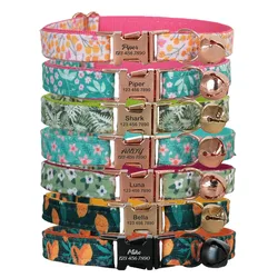 Stack of colorful pet collars with floral patterns and metal buckles, each engraved with names like Piper, Shark, Andy, Luna, Bella, and Mike, along with a contact number. Each collar has a small bell attached.