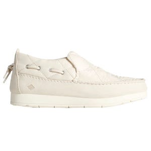 A cream-colored slip-on shoe with quilted stitching, featuring decorative lacing details and a rubber sole for casual wear.