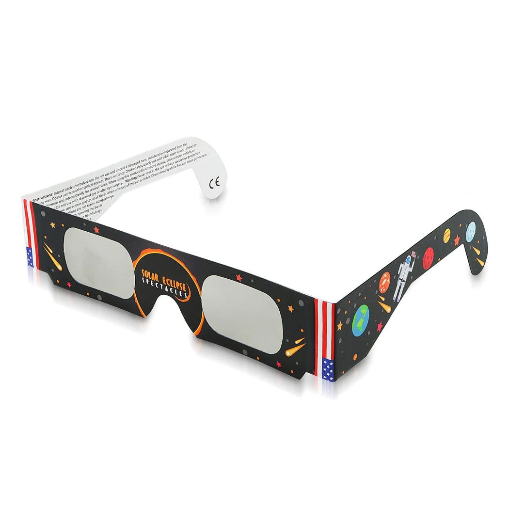 A pair of paper solar eclipse glasses with a cosmic design, including stars, planets, and an American flag motif on the frame.