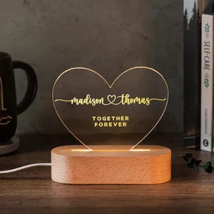 Heart-shaped LED acrylic night light with engraved names \“Madison\“ and \“Thomas\“ and the words \“Together Forever,\“ mounted on a wooden base.