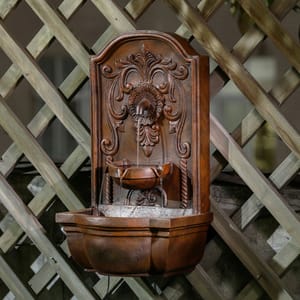 A decorative wall-mounted fountain features an ornate carved design and a small basin, set against a lattice backdrop.