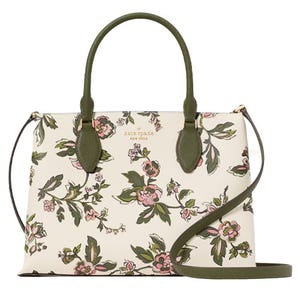 A floral-patterned handbag with green handles and a matching strap, showcasing a white background with pink and green floral designs. Brand name is visible at the top center.