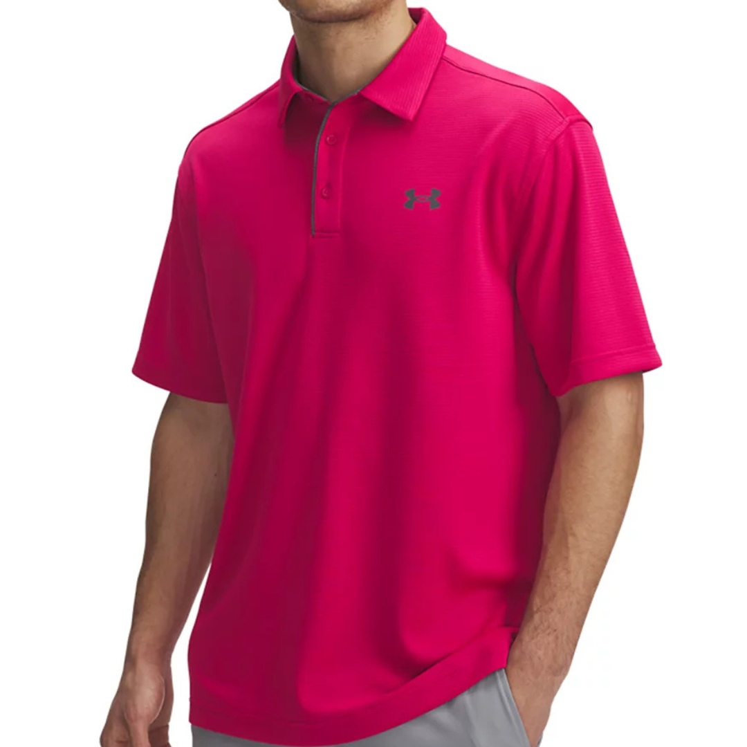 A man is wearing a bright pink Under Armour polo shirt with a subtle logo on the chest and paired with light gray pants.