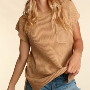 A woman wearing a tan, short-sleeved knit top with a pocket, paired with blue jeans.