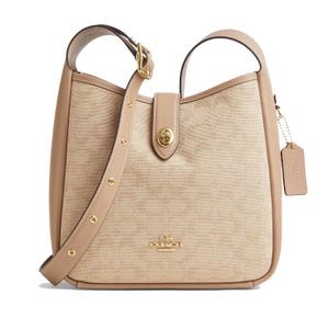 A beige Coach shoulder bag with a leather strap, gold-tone hardware, a turn-lock closure, and a signature tag.