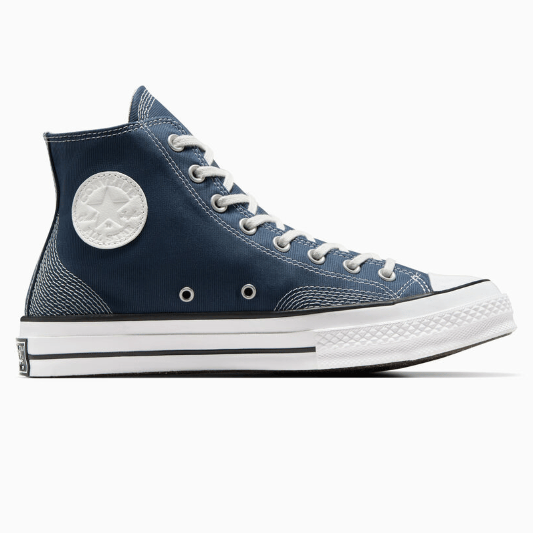 A high-top navy blue canvas sneaker with white rubber soles and toe cap, featuring metal eyelets.