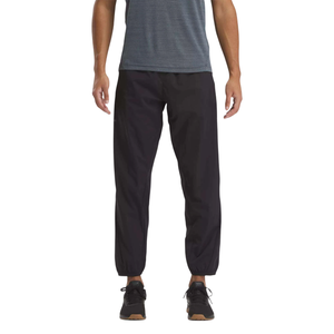 Man wearing black jogger pants with elastic cuffs, paired with a blue shirt and black sneakers.