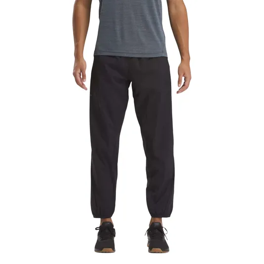 Man wearing black jogger pants with elastic cuffs, paired with a blue shirt and black sneakers.