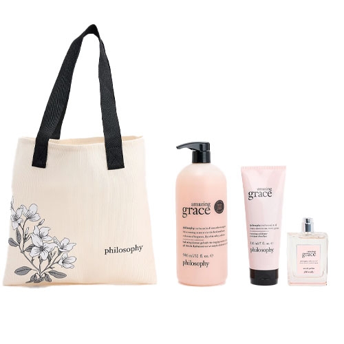 A cream-colored tote bag with flower design and black handles accompanies a set of Philosophy \“Amazing Grace\“ products: a body lotion, perfumed body cream, and eau de toilette spray.