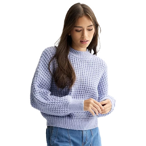A woman wears a light purple knitted sweater with a waffle texture and blue jeans.