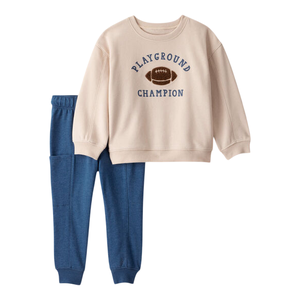 Beige sweatshirt with \“PLAYGROUND CHAMPION\“ text and a football graphic, paired with blue sweatpants.