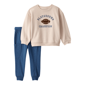 Beige sweatshirt with \“PLAYGROUND CHAMPION\“ text and a football graphic, paired with blue sweatpants.