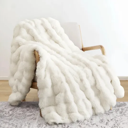 A white faux fur blanket with a textured, wavy pattern is draped over a wooden armchair on a light-patterned rug.