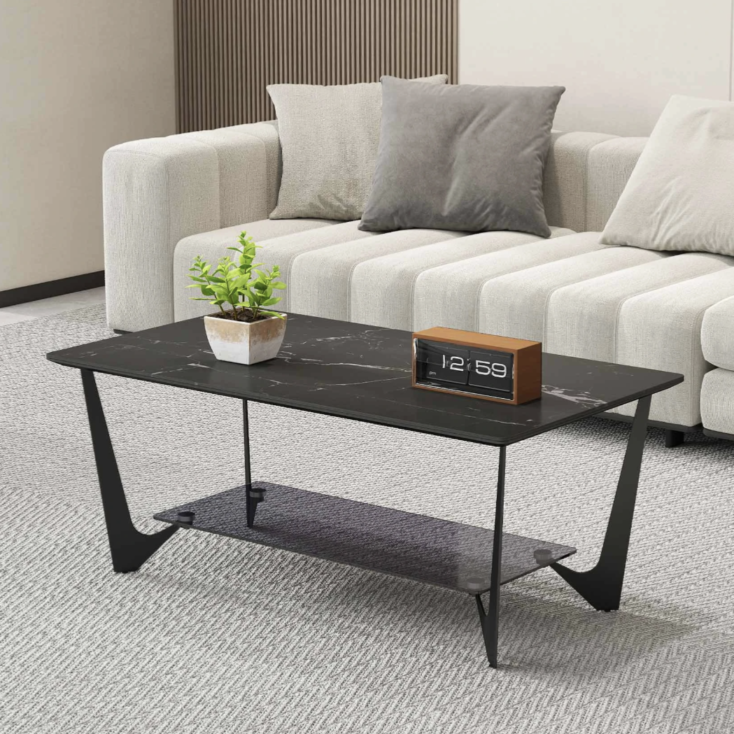 A modern living room setup featuring a black marble coffee table with a minimalist design, displaying a small potted plant and a digital clock. A light-colored sectional sofa with gray and beige cushions is in the background.
