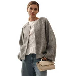 A gray, boxy, open-front jacket with relaxed sleeves, worn over a white blouse and paired with blue jeans, accessorized with a small beige handbag.