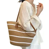 A woman is carrying a straw tote bag with brown and white stripes, featuring leather straps, while wearing a light, flowy, long-sleeve blouse.