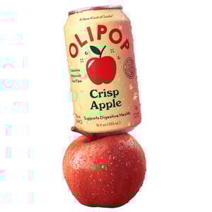 A can of OLIPOP Crisp Apple soda, described as a new kind of soda supporting digestive health, is balanced on a dewy red apple. The can contains 12 fl oz (355 mL) and is non-GMO with 5g of sugar per can.