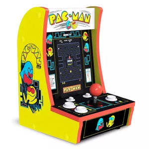 A miniature Pac-Man arcade game features a retro design with bright yellow sides, colorful graphics of Pac-Man and ghosts, and includes a joystick and buttons for gameplay, mimicking classic arcade machines.