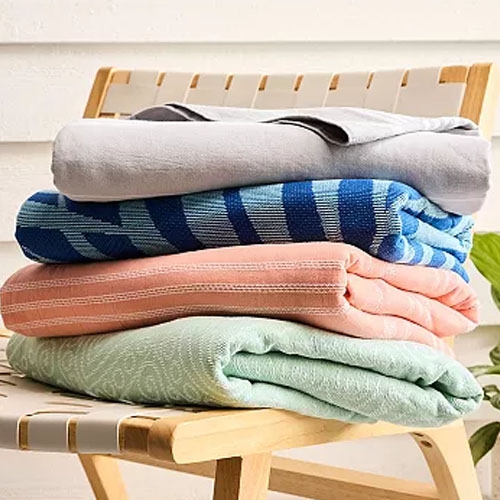 A stack of folded blankets in various colors and patterns, including gray, blue striped, pink, and mint green, resting on a wooden chair.