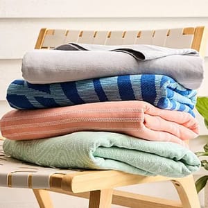 A stack of folded blankets in various colors and patterns, including gray, blue striped, pink, and mint green, resting on a wooden chair.