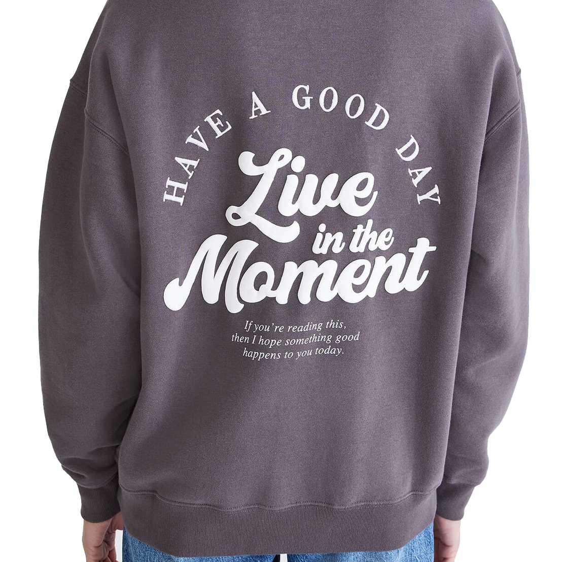 Dark grey oversized sweatshirt with \“HAVE A GOOD DAY\“ and \“Live in the Moment\“ printed in white on the back. A smaller message reads, \“If you're reading this, then I hope something good happens to you today.\“