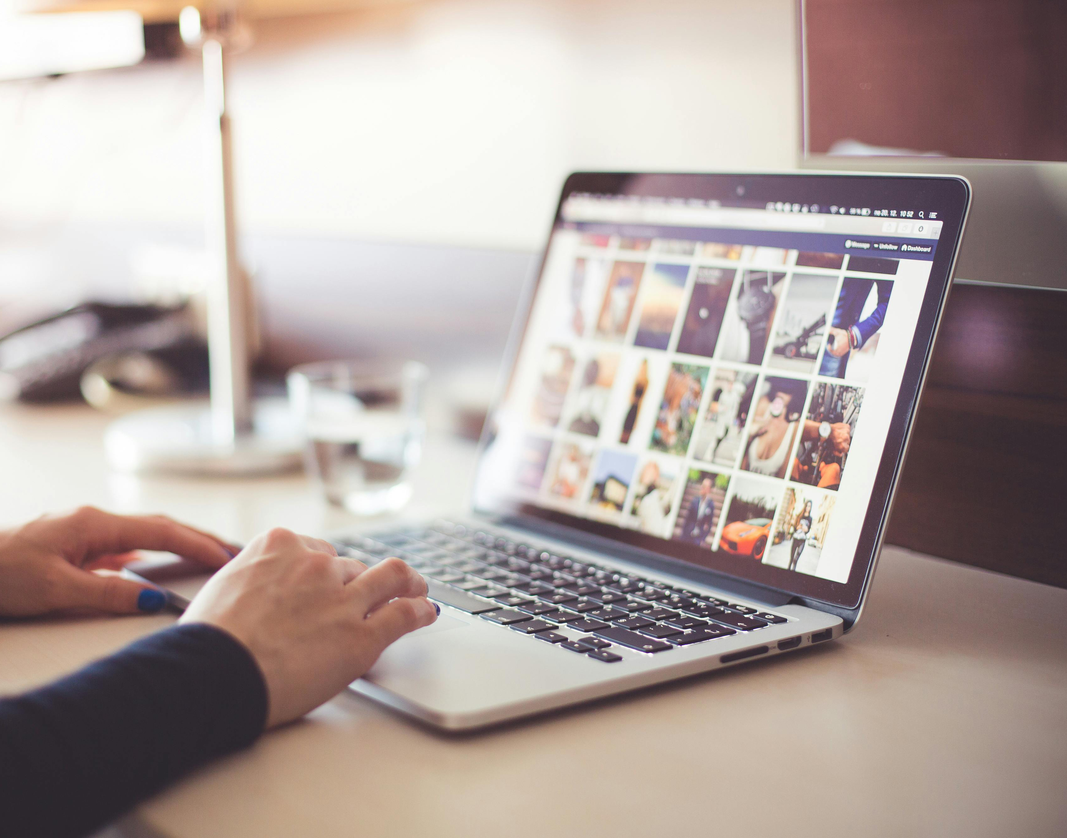 A laptop displaying a photo gallery and a person's hands typing on it.
