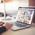 A laptop displaying a photo gallery and a person's hands typing on it.