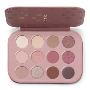An eyeshadow palette with twelve shades labeled as Dew Drops, Moonflower, Whimsical, Belle, Vintage Peony, Shimmering Petals, Rustic Rose, Full Bloom, Dusty Lilac, Romance, Fall Petals, and Gothic Garden, housed in a pink case with the brand name UBC.