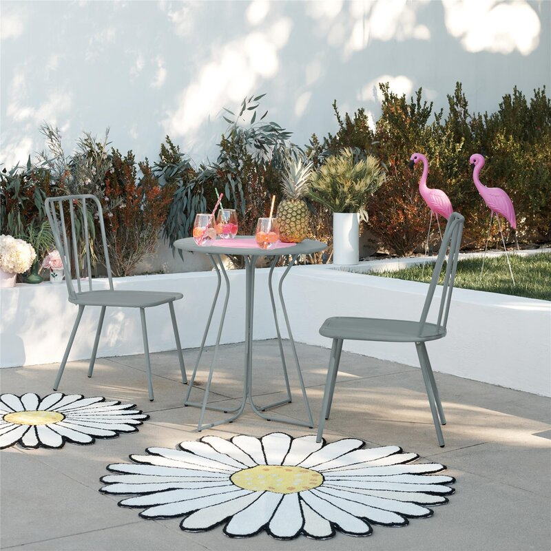 Outdoor patio set comprising a round table and two chairs in a garden with two pink flamingo decorations and large daisy-shaped rugs.