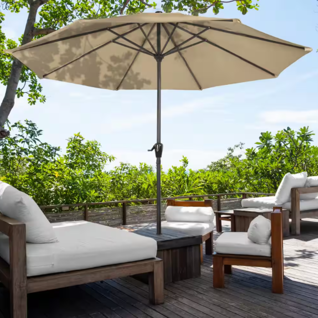 A 9-foot beige patio umbrella with a central pole and a crank handle, set up on a wooden deck among cushioned outdoor furniture.