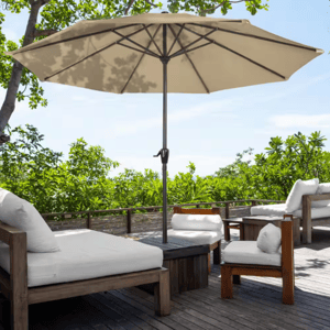 A 9-foot beige patio umbrella with a central pole and a crank handle, set up on a wooden deck among cushioned outdoor furniture.