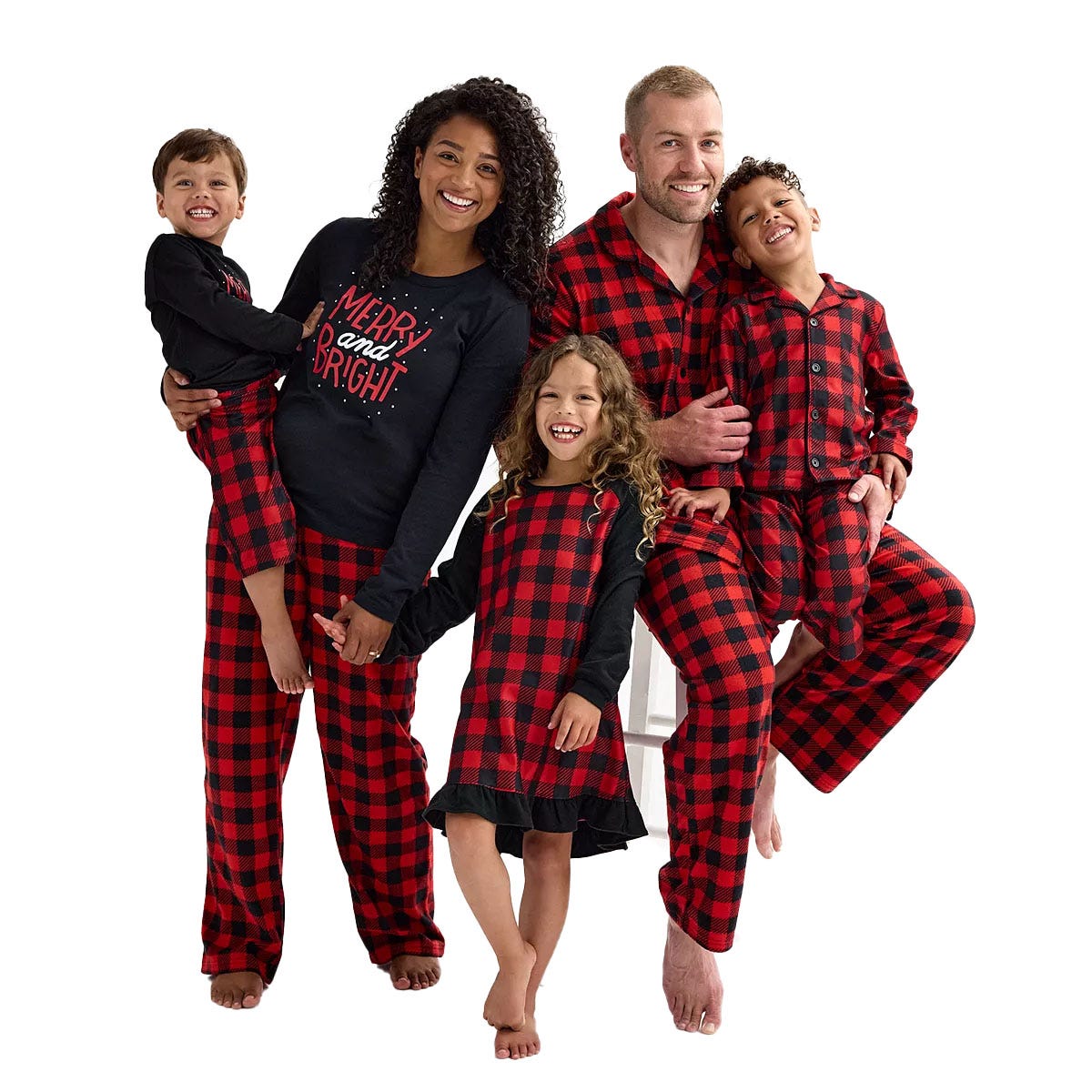 A family of five wears matching red and black plaid pajamas. The dad and one child wear long-sleeve button-up sets, the mom wears a \“Merry and Bright\“ shirt with matching pants, and two children wear a nightgown and full matching set.