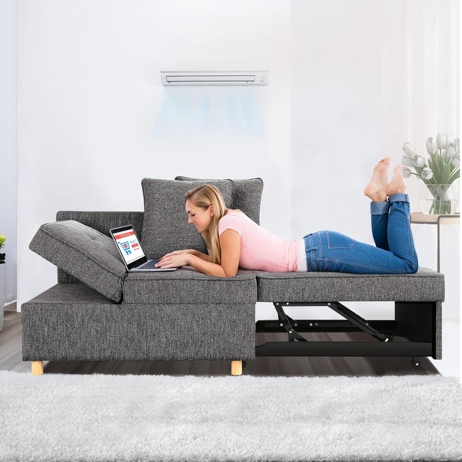 Modular gray sofa with storage compartment, featuring adjustable backrest; woman lying on it using a laptop.